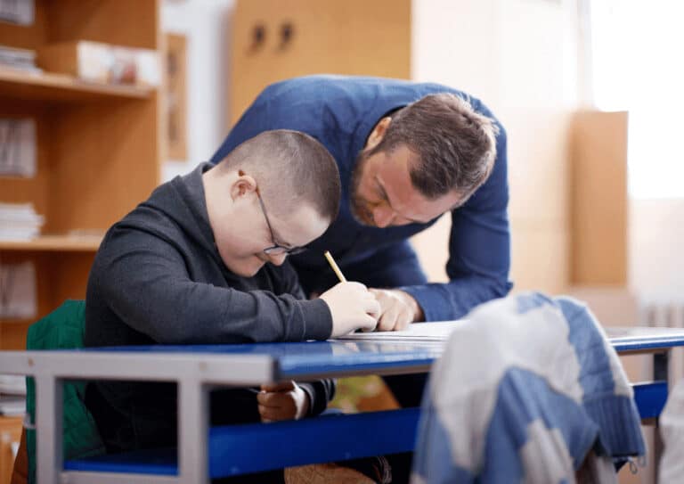 Sozialassistent unterstützt Kind mit Down-Syndrom bei Hausaufgaben